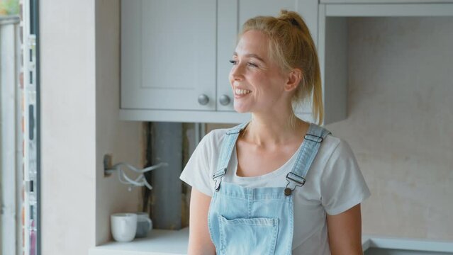 Portrait of smiling woman wearing dungarees renovating kitchen at home - shot in slow motion