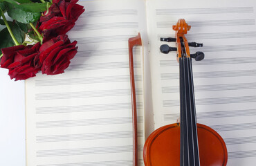 Violin, bow, music book and a bouquet of red roses.