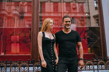 Young adult European couple in black clothes standing in city walking, traveling on honeymoon. Pretty redhead Irish woman dating Hispanic man. Romance, relationship. Cheerful guy with wife outside.