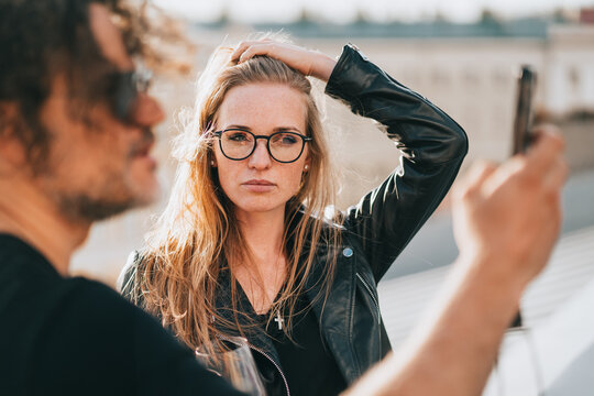 Serious young redhead woman with hipster boyfriend making selfie on rooftop. European couple reading news on phone. Financial troubles. Relationship difficulties. Woman in glasses frustrated. Model