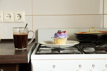 Obraz na płótnie Canvas One muffin stands on a gas stove and next to it is a cup of coffee in the kitchen for breakfast at home, dessert
