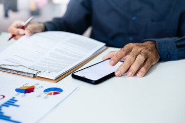 Asian businessman using smart phone to searching stocks market data, Successful business people read on paperwork report and analysis investment plan with chart on paperwork, Close-up view