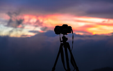 Photographing the sunrise. Silhouette of a professional camera on a tripod against amazing sunrise sky in background.
