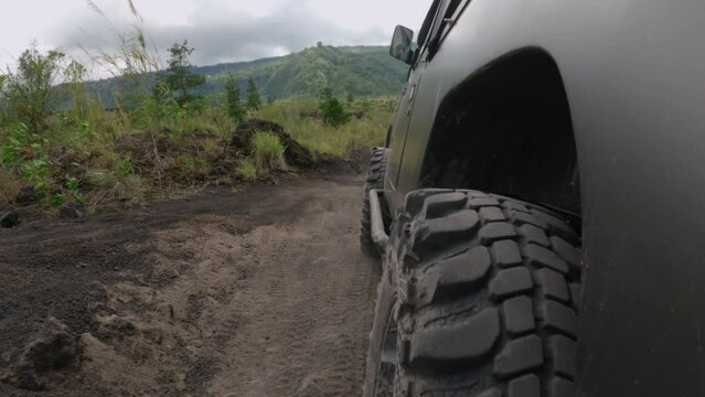 Close-up of the wheels of an SUV driving on a dusty road during a green mountain expedition. Left side of a dark car driving off-road. Adventure automobile tires for increased cross-country ability