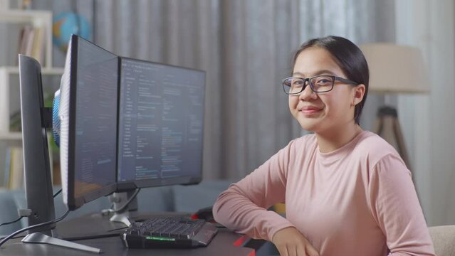 Asian Teen Girl Programmer Smiling To Camera While Creating Software Engineer Developing App, Program, Video Game On Desktop Computer At Home. Terminal With Coding Language 
