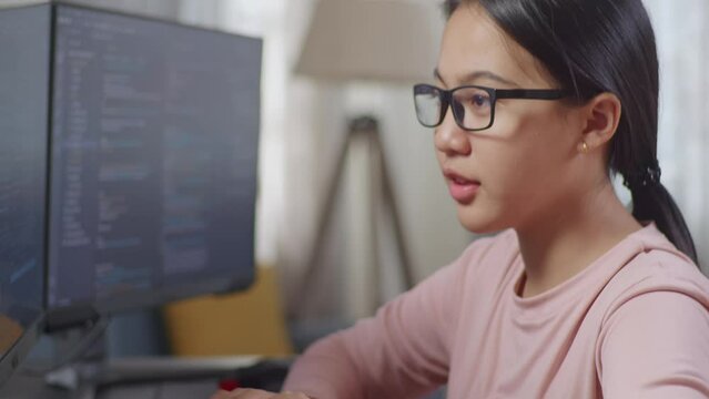 Close Up Of Asian Teen Girl Programmer Smiling To Camera While Creating Software Engineer Developing App, Program, Video Game On Desktop Computer At Home. Terminal With Coding Language 
