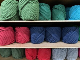 Colorful yarn balls for knitting being arranged on a shelf in a accessories store.