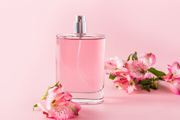 Beautiful bottle of cosmetic spray or perfume on a pink background with astromeria flowers. front...
