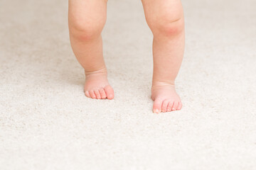 Baby barefoot on light soft carpet. Closeup. First steps. Front view.