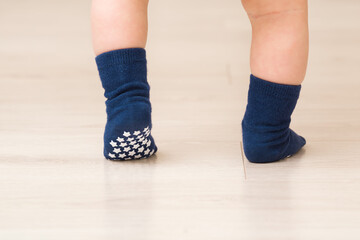 Baby boy legs on light beige wooden floor. Feet in dark blue anti slip socks. Infant first steps....