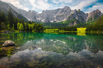 Green forest and clean alpine lake with high mountains, Italy