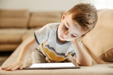 Youngsters and technology addiction. A young boy is wasting his time by watching videos on tablet at home.