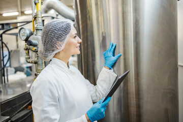 A milk processing factory expert is monitoring milk tank while holding tablet in her hands.