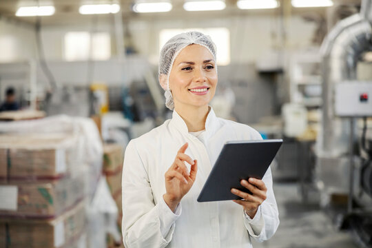 A happy food factory inspector is monitoring works on tablet while walking around factory.