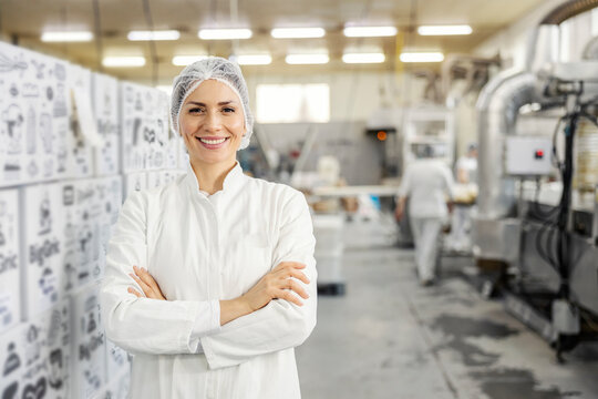Portrait of a food factory worker standing in facility with arms crossed and smiling at the camera.
