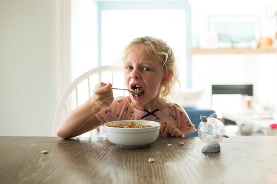 Blonde Girl Missing Front Tooth Eats Cereal at Bright Kitchen Table