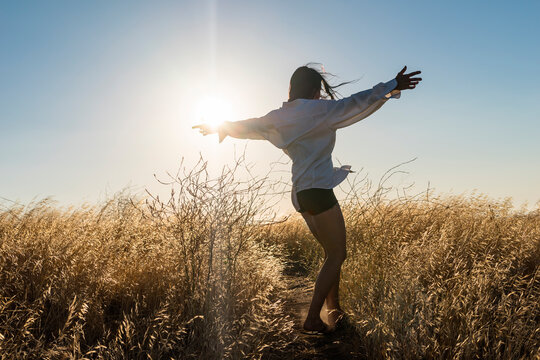 Woman dancing in a field of golden grass in sun drenched hills of California.