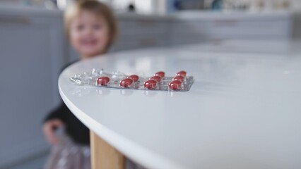 Caucasian Toddler Girl Picking Up Blister Pack of Pills Medicine Left Unattended on Table by Unwary...