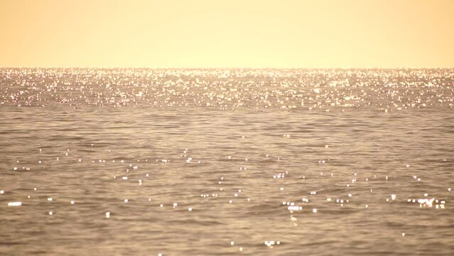 Abstract aerial sea summer ocean sunset nature background. Small waves on azure water surface in motion blur with golden bokeh lights from sun. Holiday, vacation and recreational concept. Slow motion