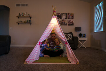Young mom reading to two three year old twins in fort in living room before going to bed, Neenah, Wisconsin, USA