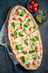 Long pizza with broccoli, tomatoes, basil and shrimp. Extra-sized Italian pizza, served on a wooden board, top view