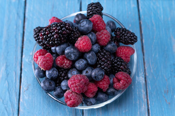 Various forest berries in a glass plate. Multi-colored berries in a saucer. Summer forest berries in a plate on the table.