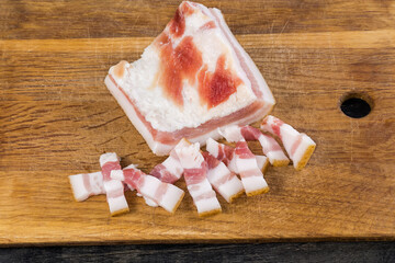 Partly sliced salted pork fatback on a wooden cutting board