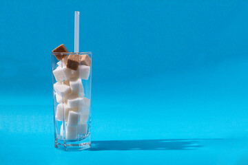 Glass with straw full of sugar and cubes on blue background. The concept of prevention of diabetes,...