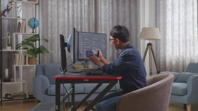 Asian Boy Programmer Looking At Smartphone Then Celebrating The Success While Creating Software Engineer Developing App, Program, Video Game On Desktop Computer At Home

