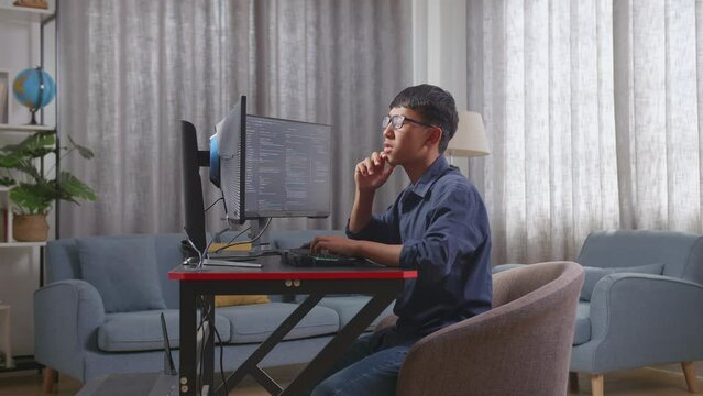Asian Boy Programmer Thinking About Something And Raising His Index Finger While Creating Software Engineer Developing App, Program, Video Game On Desktop Computer At Home
