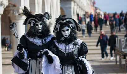 a couple in period costumes stroll in front of the Venice lagoon