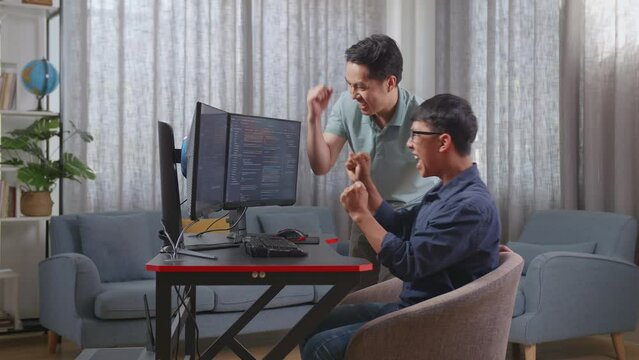 Happy Asian Boy And Male Celebrating Succeed Creating Software Engineer Developing App, Program, Video Game On Desktop Computer At Home. Terminal With Coding Language

