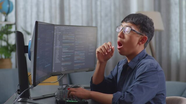 Asian Boy Programmer Yawning While Creating Innovative Software Engineer Developing App, Program, Video Game On Desktop Computer At Home. Terminal With Coding Language 
