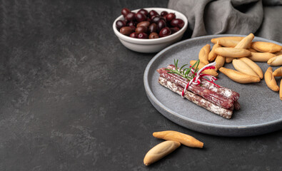 Plate with Spanish sticks of mini fuet and picos - bread sticks and bowl with dark olives on the...