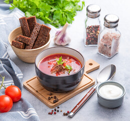 Borsch soup with beetroot,  meat and sour cream in a bowl on a light background with croutons and fresh herbs.