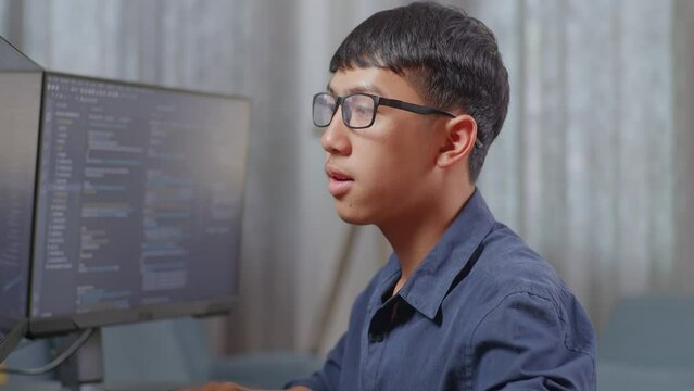 Close Up Of Asian Boy Programmer Smiling To Camera While Creating Software Engineer Developing App, Program, Video Game On Desktop Computer At Home. Terminal With Coding Language 
