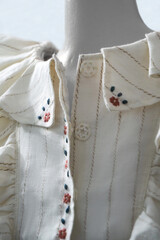 Part of the white linen dress with embroidered patterns, beautiful details of the dress close-up. Selective selective focus