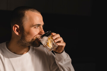 Attractive young man drink lemonade or water with lemon and ice cube. Male in white long sleeve...