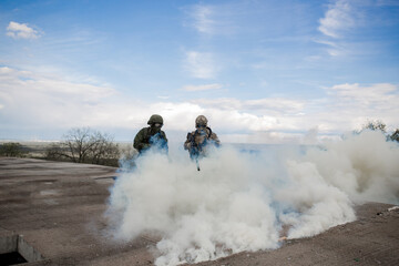 Two soldiers in the war shoot from a machine gun in a smoke curtain on the roof of a building