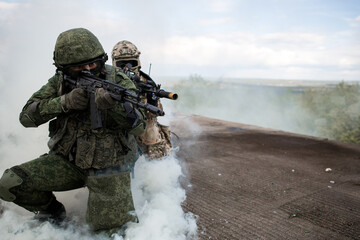 Two soldiers in the war shoot from a machine gun in a smoke curtain