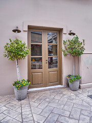 Vintage double pale brown painted door and potted laurel plants by the sidewalk. Travel to Athens, Greece.