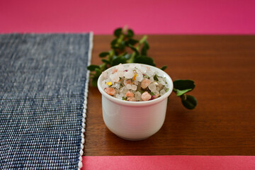 colorful mountain herb salt in a small white container on a dark wooden plate on a blue white and pink background, copy space