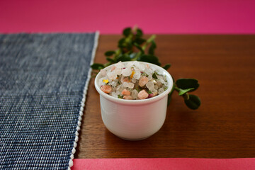 colorful mountain herb salt in a small white container on a dark wooden plate on a blue white and pink background, copy space