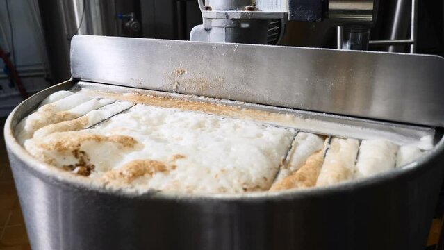 Beer brewing process. Brewing foam in tank. Beer being made in craft brewery, close up. Close up top view kettle with beer inside, flowing beer. Brewing technology. Brewery. Boiling flow of dark brown
