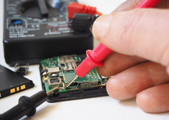 IT technician repairing broken mobil phone. Troubleshooting on the smartphone's motherboard. Focused on probes.