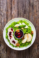 Fresh salad - goat cheese, pear, jam, lettuce and walnuts on wooden background

