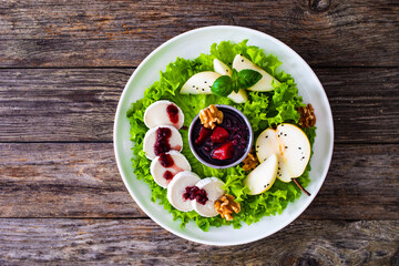 Fresh salad - goat cheese, pear, jam, lettuce and walnuts on wooden background

