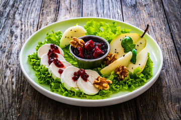 Fresh salad - goat cheese, pear, jam, lettuce and walnuts on wooden background


