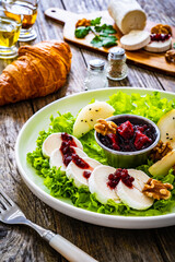 Fresh salad - goat cheese, pear, jam, lettuce and walnuts on wooden background

