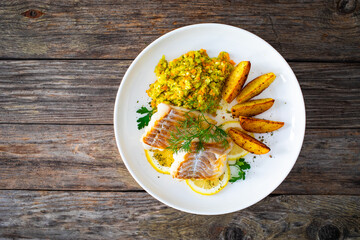 Fish dish - fried cod with baked potatoes and fresh vegetables on wooden table
